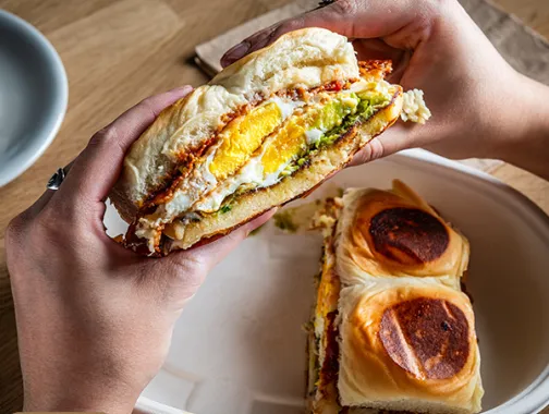 Hands holding a breakfast sandwich at Café Unido.
